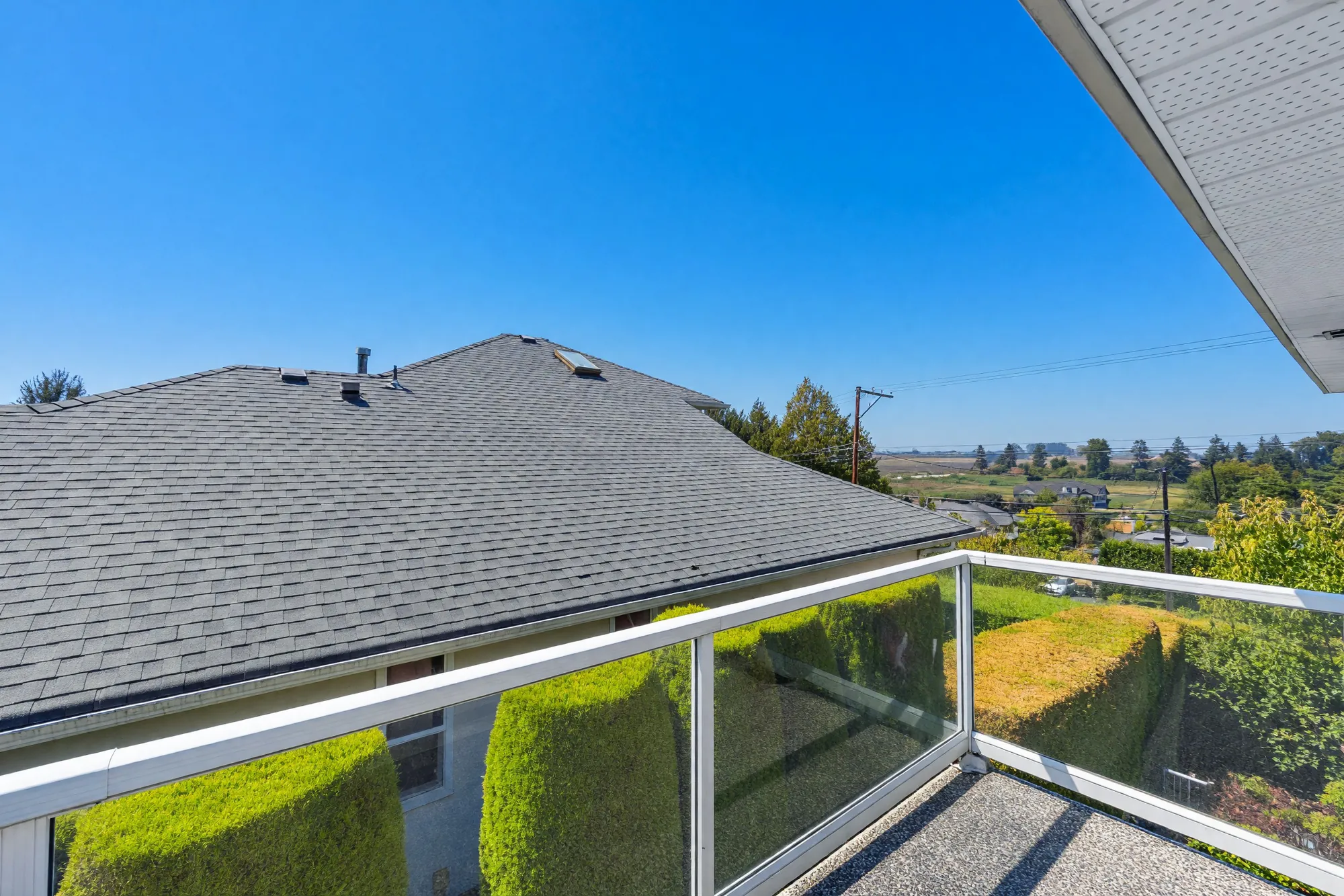 The small balcony over the main roof: glass railings, the shingled roof, hedges and fields beyond