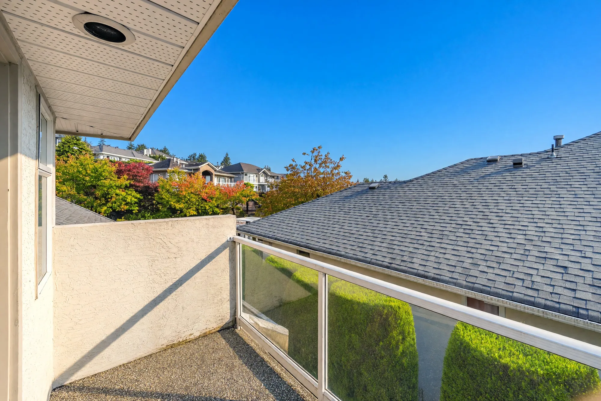 The small balcony toward its stucco privacy wall, the roof below, trees beyond