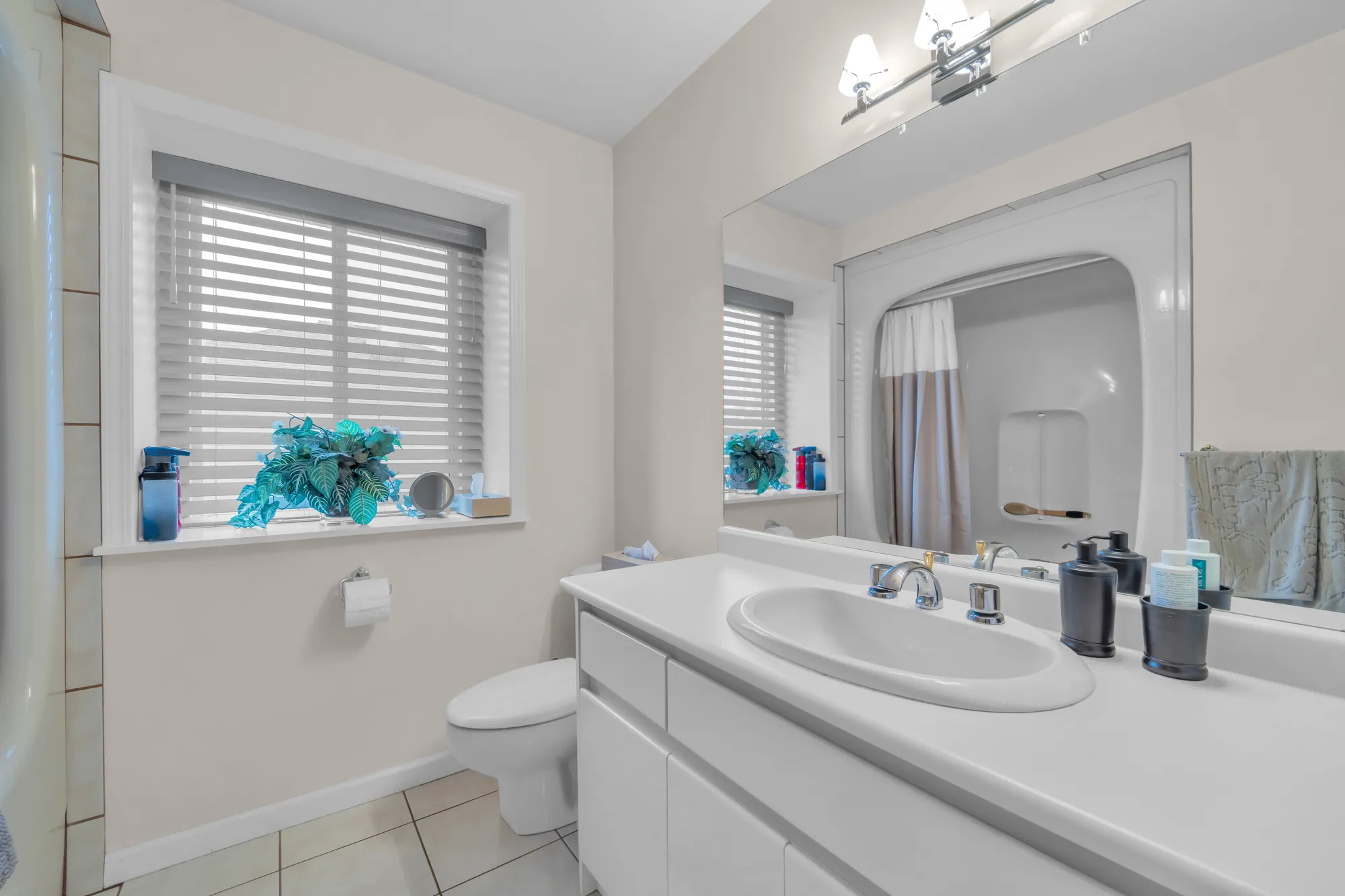 The upper bathroom: a white vanity, a toilet, a window, a tub with a shower curtain reflected in the mirror