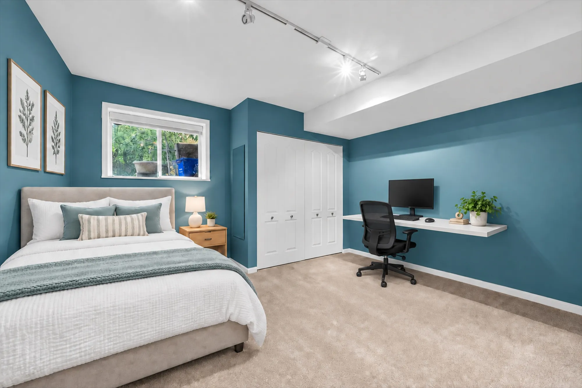 The second lower bedroom virtually staged: a bed with white and blue linen, a night table and lamp, a floating desk and chair, two botanical prints on blue walls, a double closet