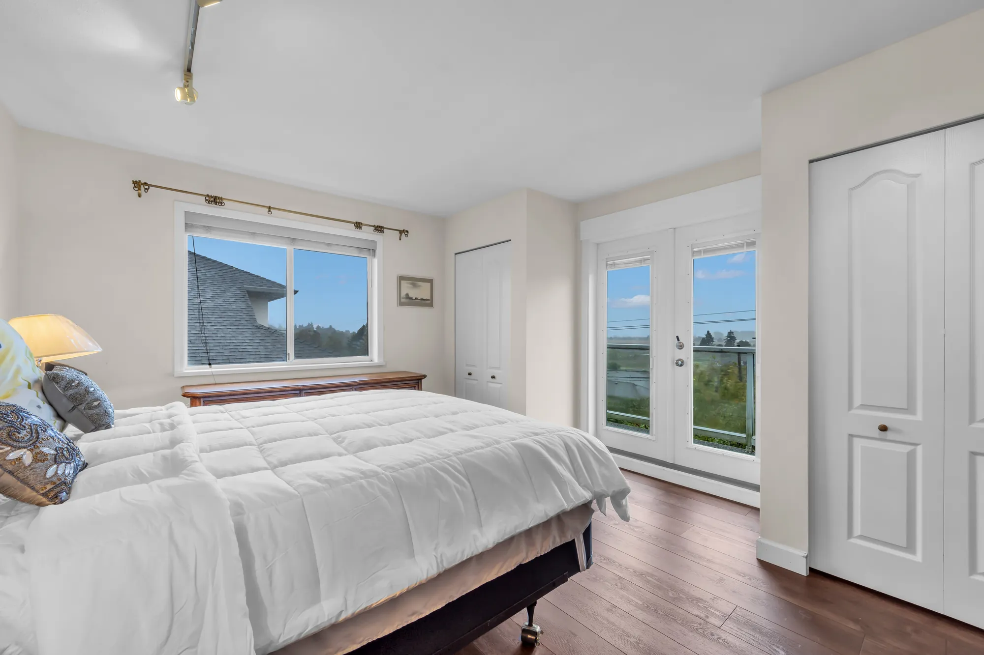 An upper bedroom: a bed with white linen, French doors to a balcony, a white closet door
