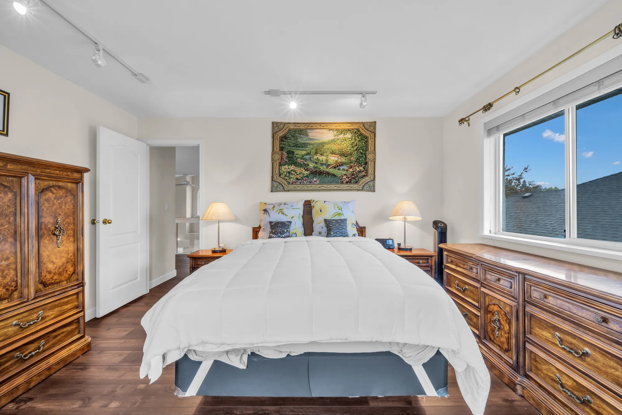 The same bedroom toward its door: the bed, an armoire and a dresser, a window