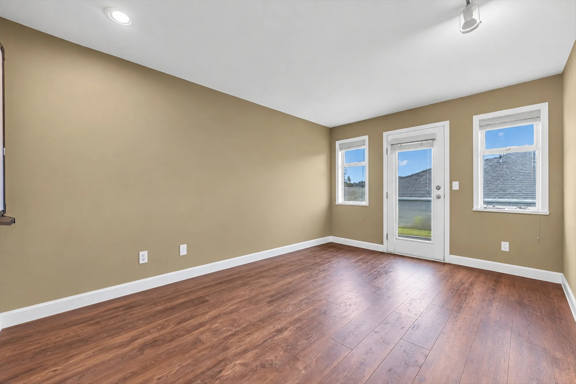 The second upper bedroom shown empty: tan walls, wood-look floors, two windows and a glass door to a balcony