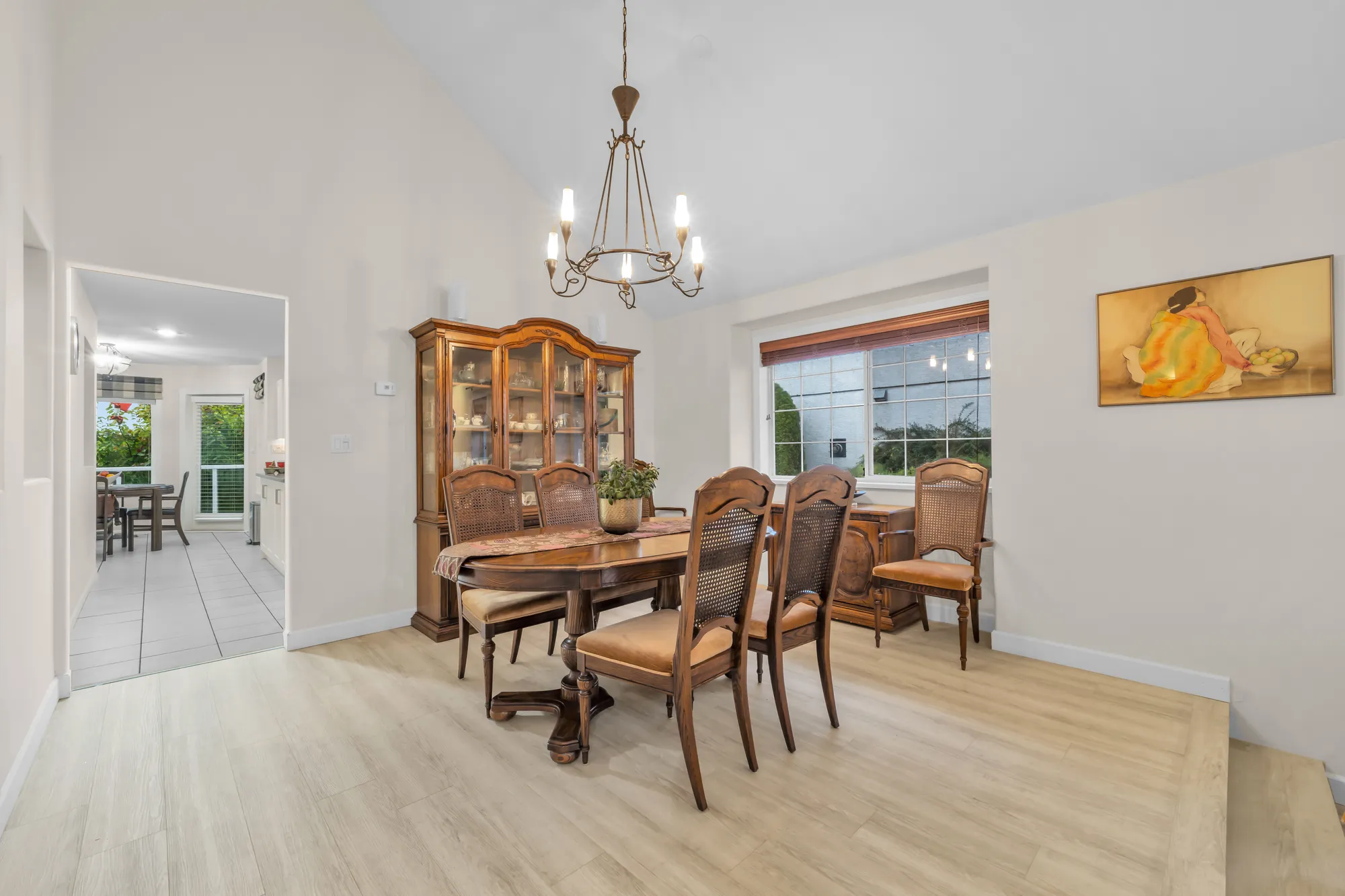 The dining room: a wood table and chairs under a chandelier, a china cabinet, a window, a vaulted ceiling