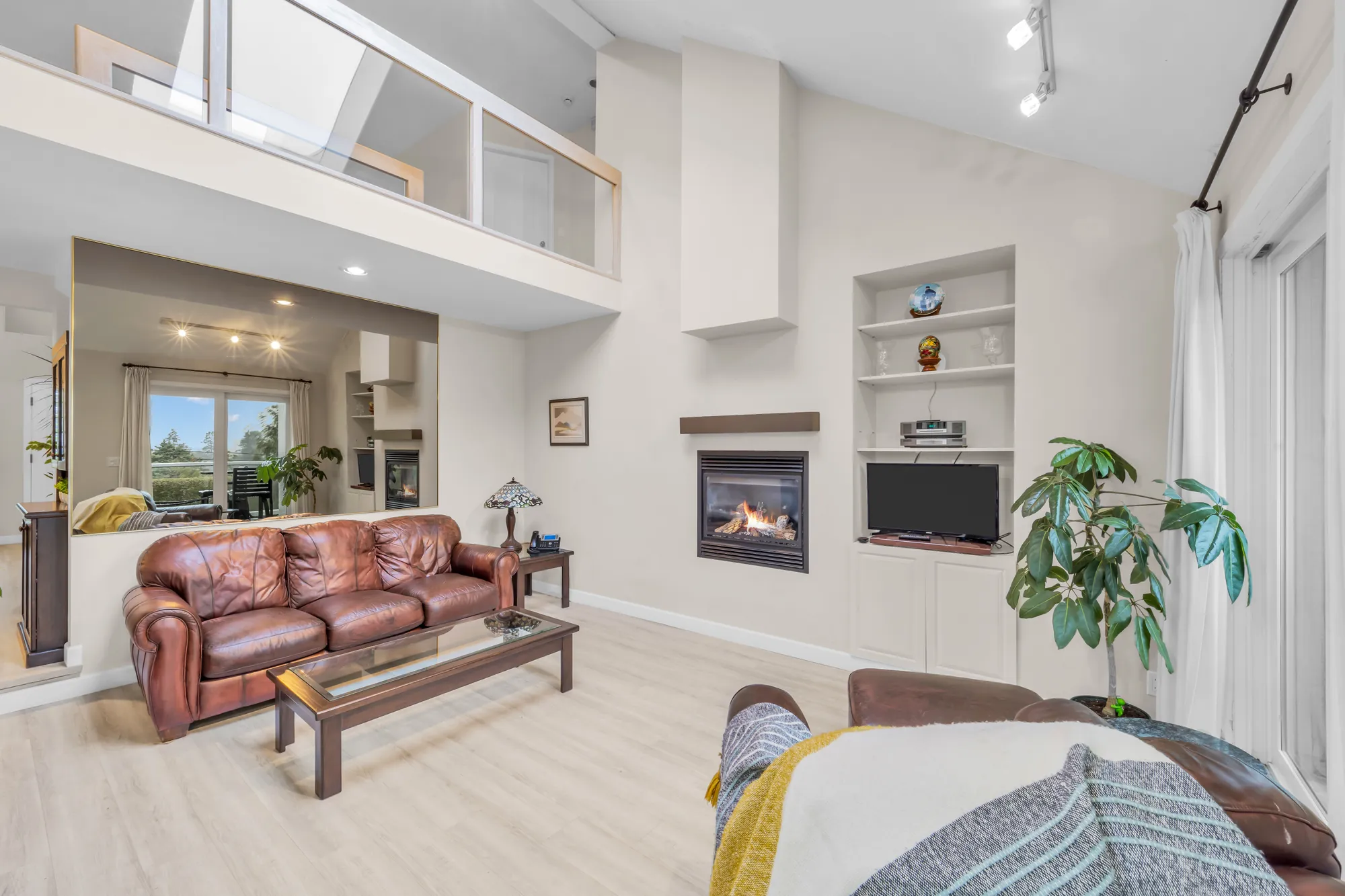 The family room: a gas fireplace with built-in shelves and a TV niche, a leather sofa, a vaulted ceiling open to the upper hall