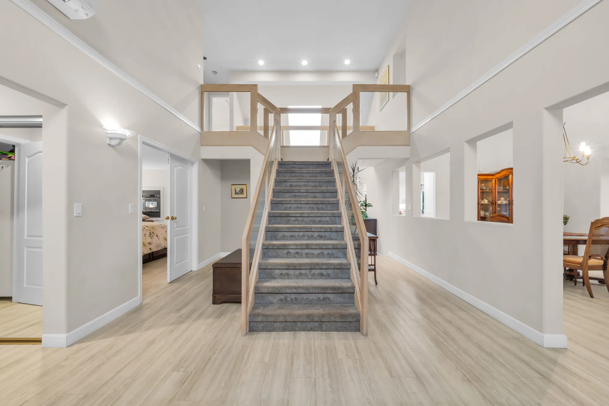 The foyer: a hall two storeys high with a carpeted stair rising to the upper floor, pale floors, doors to the rooms on either side