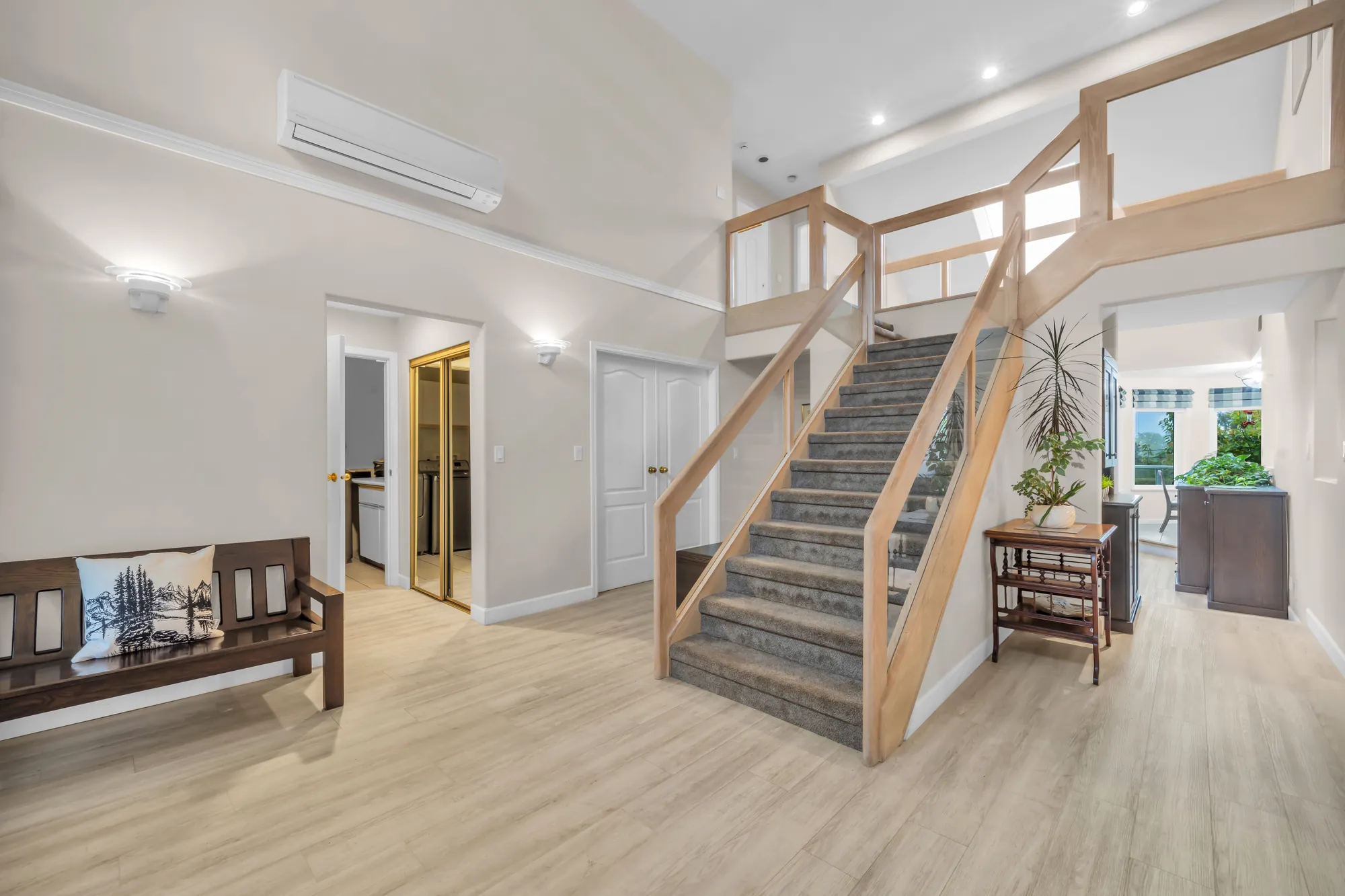 The foyer from the other side: the stair and its wood railing, a bench, doors to the bedroom wing, an air conditioner high on the wall