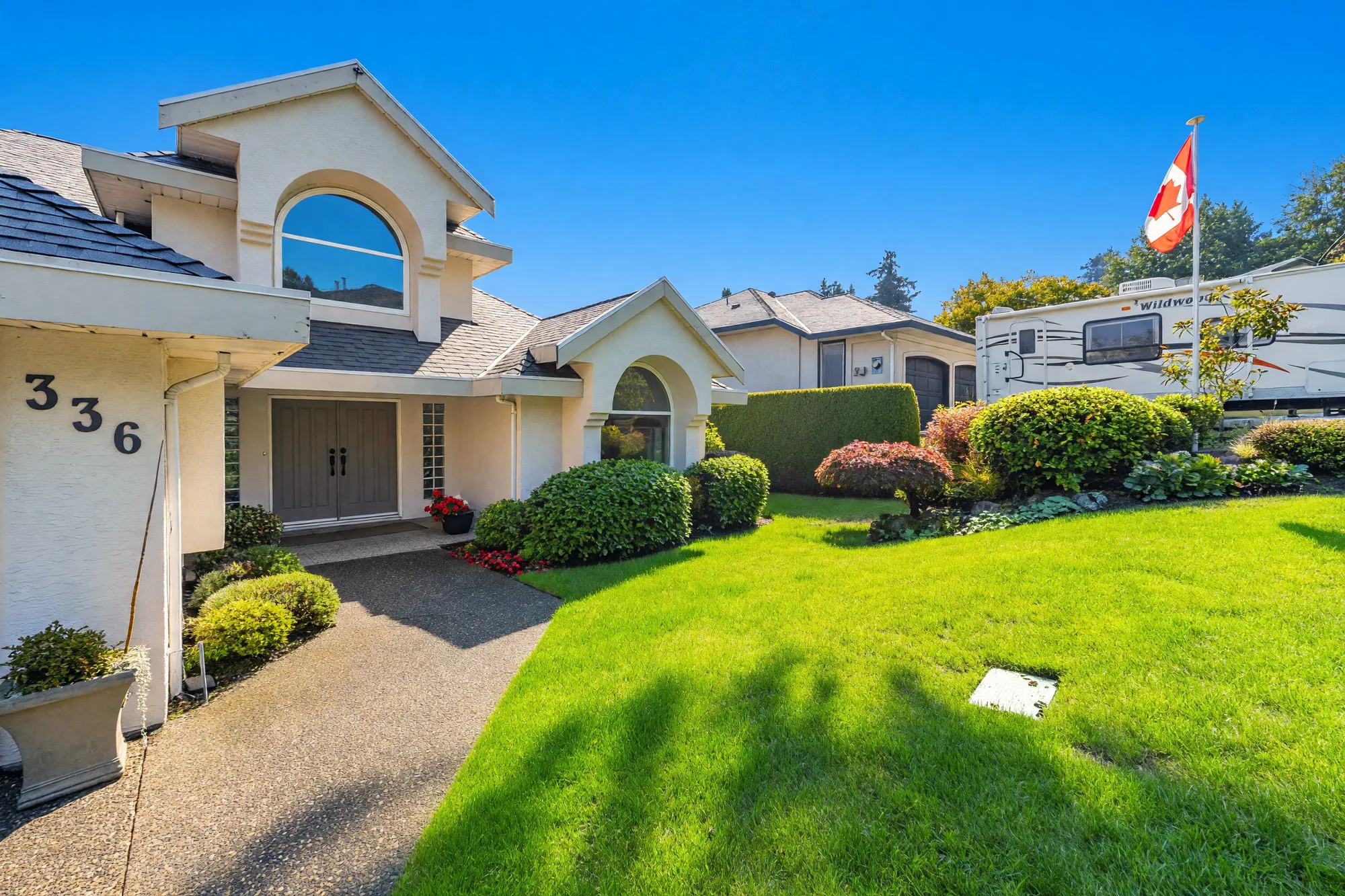 The entry: a pair of dark front doors under an arched gable, glass-block panels beside them, the number 336 on the wall, a lawn and clipped shrubs