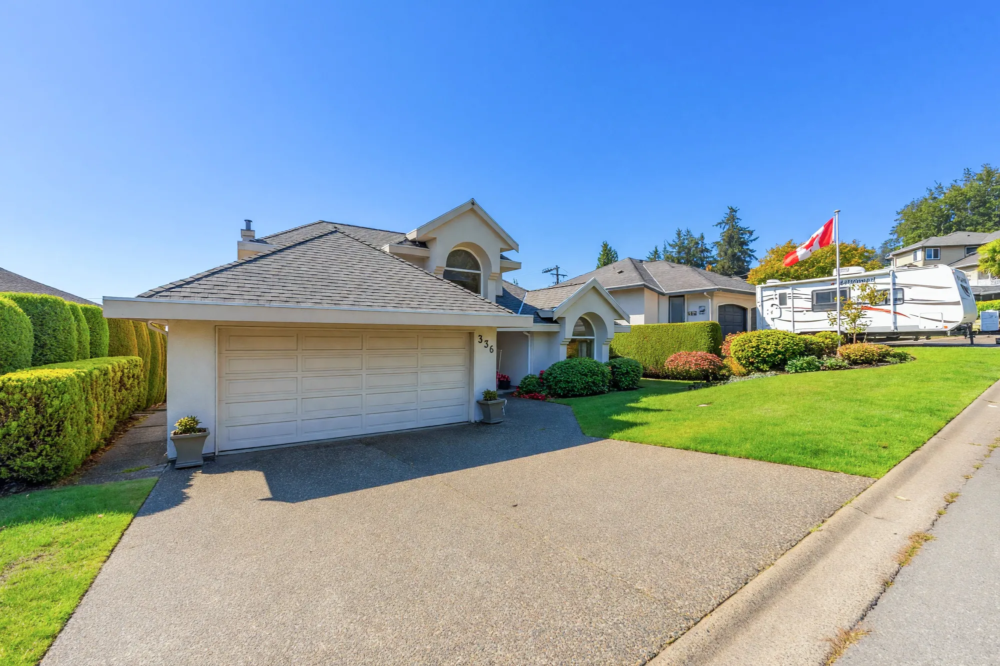 The double garage and the driveway, a hedge along the side of the lot, the lawn at the right