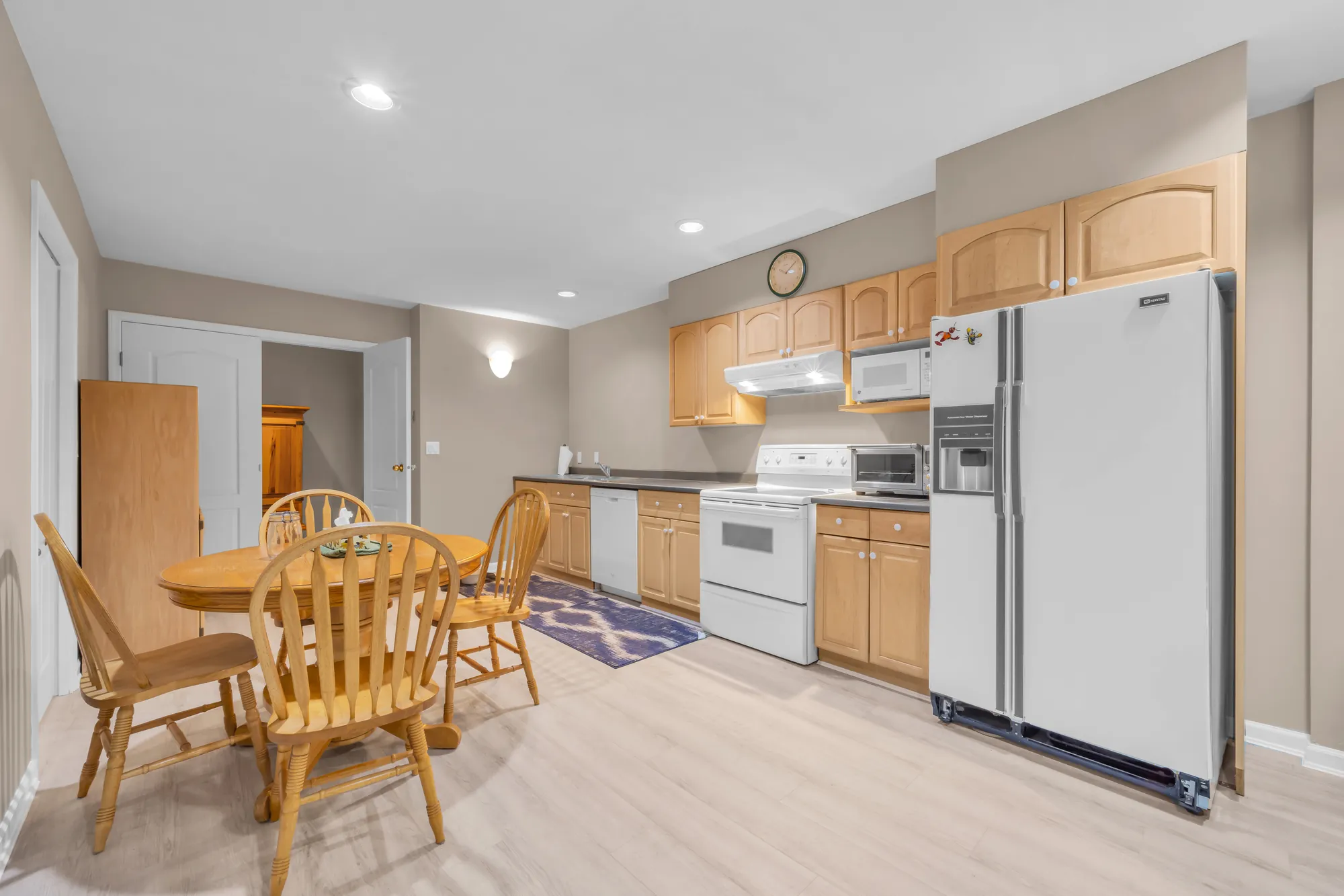 The lower floor&rsquo;s eat-in kitchen: maple cabinets, a white fridge and range, a round wood table and chairs