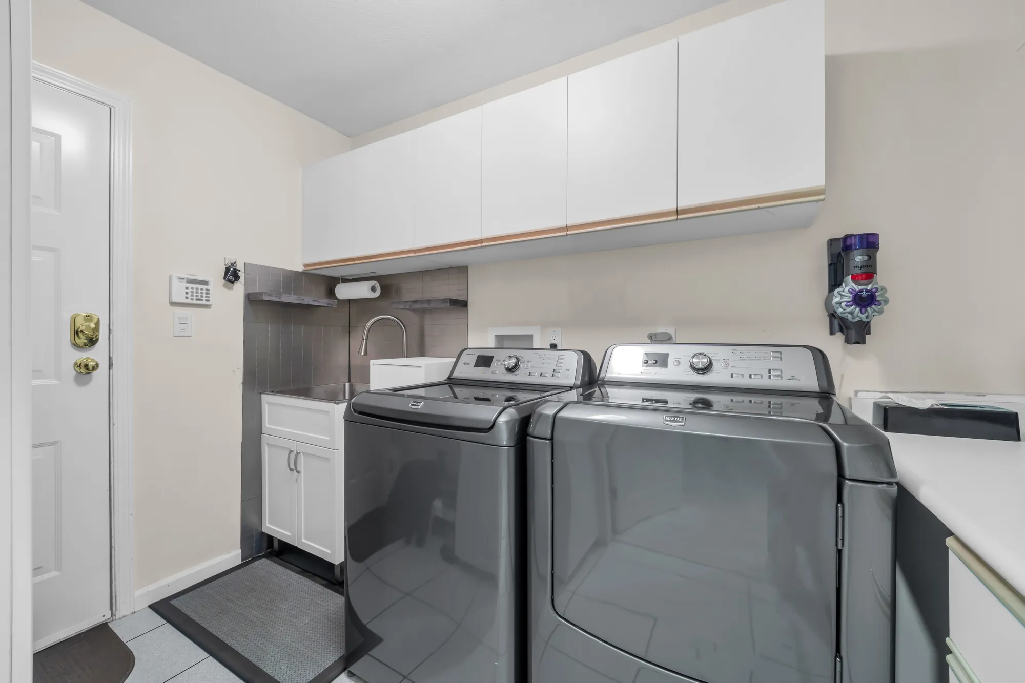 The laundry room: a washer and dryer, a sink, cabinets above, a door