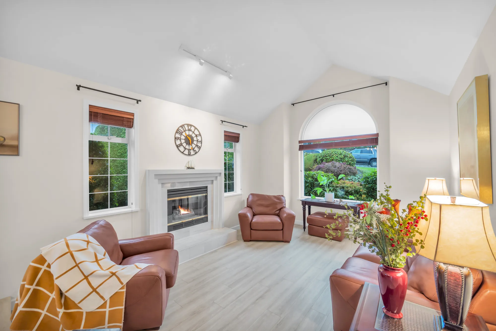 The living room: a gas fireplace in a white surround, an arched window and a window with blinds, leather sofas and armchairs, pale floors