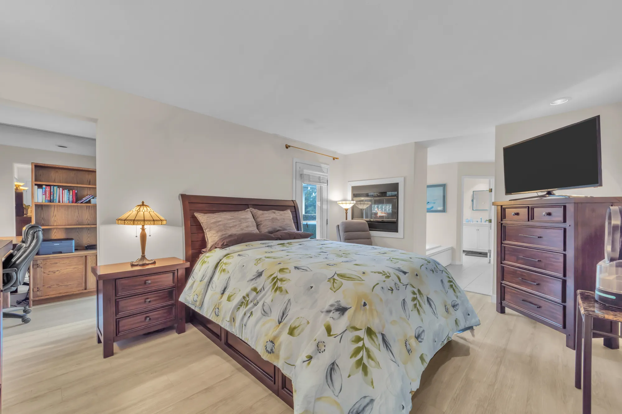 The primary bedroom toward the office and the bathroom, a TV on a tall dresser