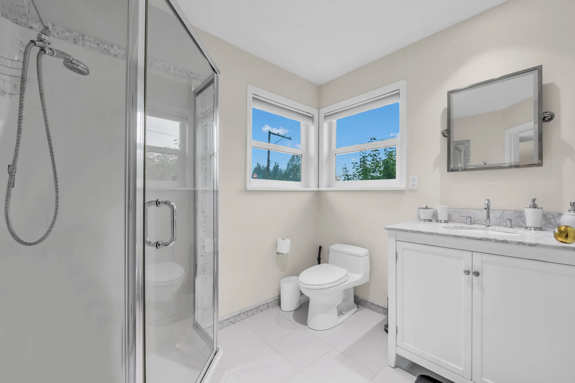 The glass shower, the toilet and a second vanity with a marble top, windows on two walls