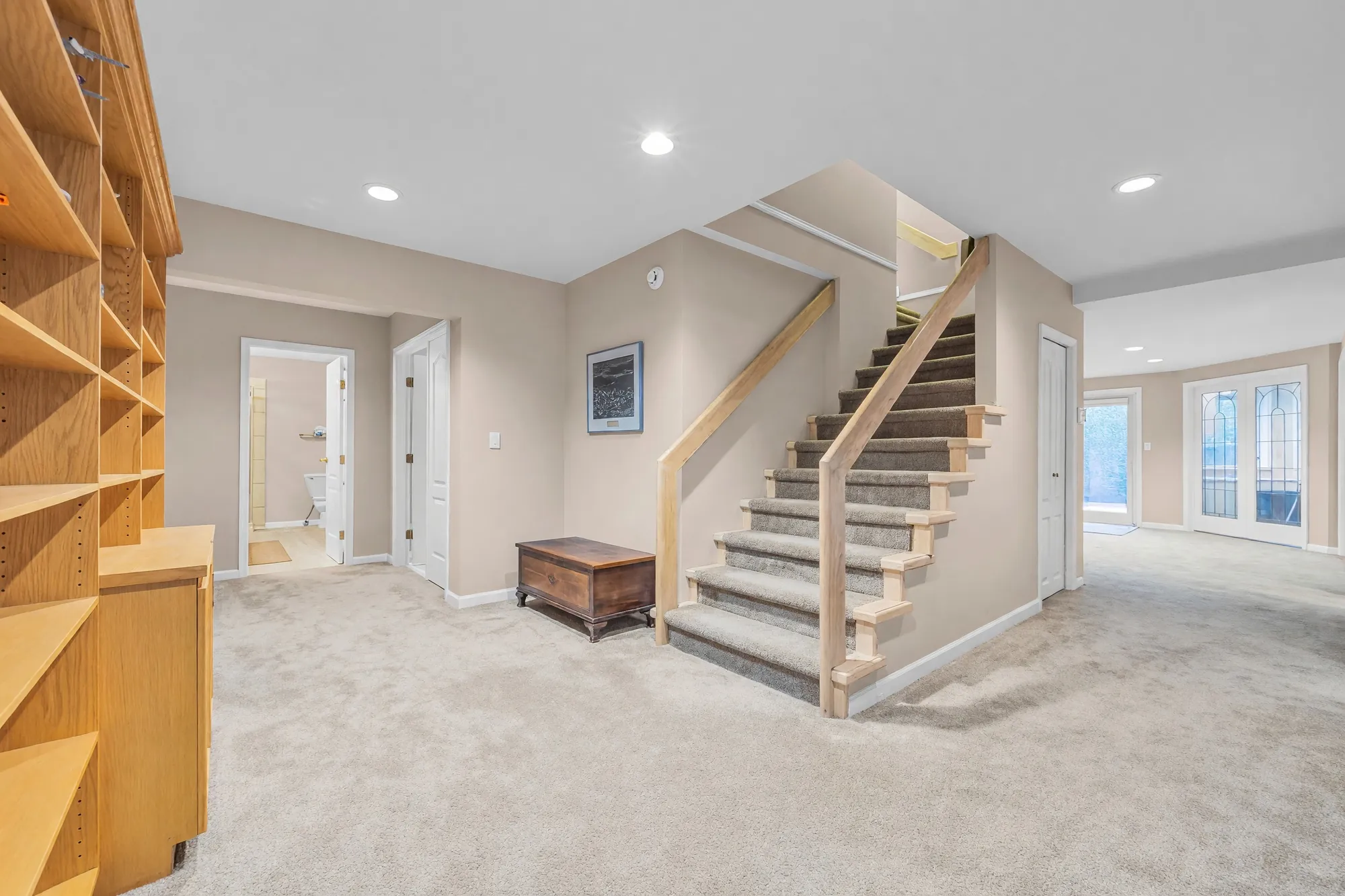 The lower hall: the stair from the main floor with carpeted treads and a wood railing, built-in shelves at the left, doors to the rooms